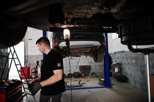 Car repair and maintenance theme. Mechanic in uniform working in auto service. photo