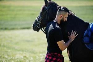 Hombre árabe de barba alta vestido de negro con caballo árabe. foto