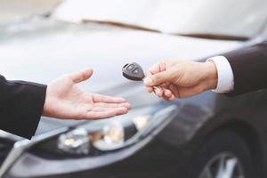 hombre de negocios mano sujetando las llaves del coche delante con un coche nuevo en el fondo. estacionamiento en frente de la casa. concepto de transporte. deje espacio de copia para escribir mensajes de texto. foto