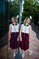 Fashionable and beautiful blonde model girl in stylish red velvet velour skirt, white blouse, posed with phone and earphones against windows of city building. photo