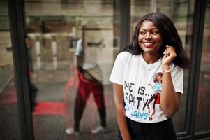 Stylish african american woman in printed t-shirt posed outdoor against window. photo