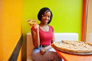 African woman with pizza sitting at bright colored restaurant. photo