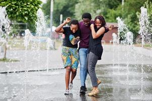 Three african american friends walking on fountains. Having fun together. photo