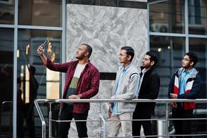 grupo de cuatro estudiantes varones adolescentes indios. los compañeros de clase pasan tiempo y hacen selfie por teléfono juntos. foto