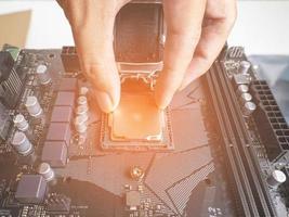 Hold the CPU handle and insert it into the CPU slot on the motherboard. It's an old motherboard, lots of dust. Put orange light on the cpu slot. There is a RAM slot next to it. There is a capacitor. photo