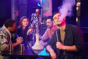 Sitting and smoking hookah. Group of friends having fun in the night club together photo