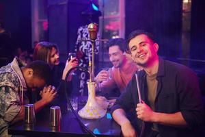 Sitting and smoking hookah. Group of friends having fun in the night club together photo