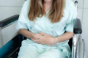 Patient hand hold stomach sit on wheelchair, sick and waiting for the doctor at the hospital photo