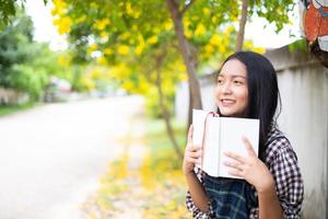 Young girl sitting on a bench reading a book under a beautiful tree. photo