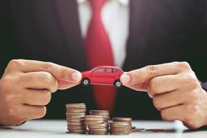 Business man in suit open hand prop up hug model of toy car on over a lot money of stacked coin insurance loan and buying car finance concept. buy and installment down payment a car. Piggy Bank saving photo