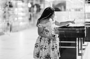 Cute small height african american girl with dreadlocks, wear at coloured yellow dress, looking aquarium at shopping center. Black and white. photo
