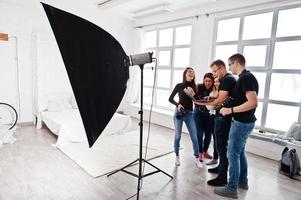 fotógrafo explicando sobre la toma a su equipo en el estudio y mirando en la computadora portátil. hablando con sus asistentes sosteniendo una cámara durante una sesión de fotos. trabajo en equipo y lluvia de ideas. foto