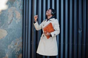 African american man with headphones, wear on hat and coat listening music on steel background. photo