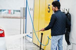 South asian man or indian male washing his white transportation on car wash. photo