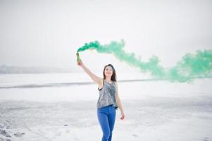 Young girl with green colored smoke bomb in hand in winter day. photo