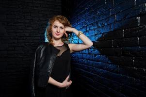 Curly hair girl at leather jacket on studio against black brick wall. photo