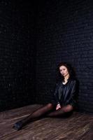 Studio portrait of sexy brunette girl in black leather jacket against brick wall. photo