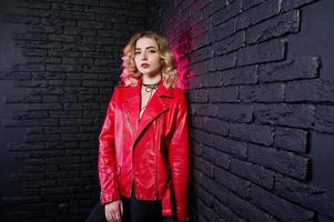 retrato de estudio de una chica rubia con una chaqueta de cuero roja contra una pared de ladrillos. foto