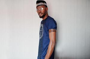 Rich african man in stylish traditional clothes and hat in glasses posed at studio against white background. photo