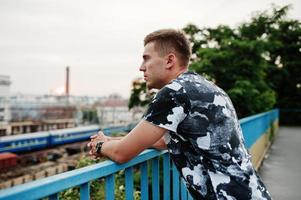 retrato de estilo de vida de un hombre guapo posando en la calle de la ciudad y mirando la estación de tren. foto