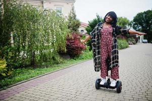 hermosa mujer afroamericana usando segway o hoverboard. chica negra en scooter eléctrico autoequilibrado de doble rueda. foto