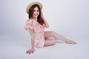 Portrait of a fashionable woman in pink dress sitting and posing with a hat on the floor in the studio. photo