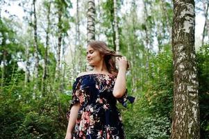 Portrait of a fabulous young girl in pretty dress with stylish curly hairstyle posing in the forest or park. photo