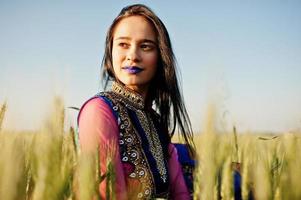 tierna niña india en sari, con maquillaje de labios violetas posada en el campo al atardecer. modelo indio de moda. foto