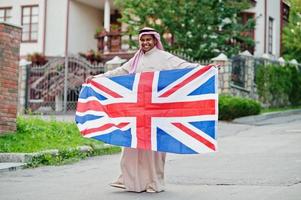 Middle Eastern arab man posed on street with Great Britain flag. England and Arabian countries concept. photo