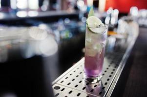 Alcoholic long violet cocktail with ice in glass at bar table. photo