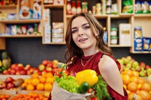 Girl in red holding different vegetables on fruits store. photo