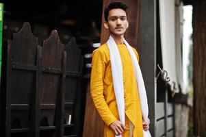 Indian stylish man in yellow traditional clothes with white scarf posed outdoor. photo