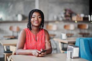 atractiva mujer afroamericana sentada en la mesa del café con el teléfono móvil en las manos. foto