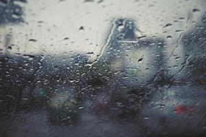 gotas de lluvia lloviznan en el parabrisas de cristal por la noche. calle bajo la fuerte lluvia. Bokeh luz trasera y semáforos en la ciudad. conduzca el automóvil con cuidado, camino resbaladizo. enfoque suave. foto