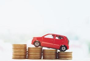 Little red car over a lot of money stacked coins with background house. for loans costs finance photo