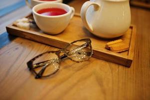 Close up photo of glasses against cup of tea at cafe table. Eyewear concept.