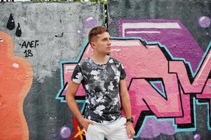 Lifestyle portrait of handsome man posing on the street of city with graffiti wall. photo