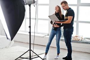 Photographer explaining about the shot to his assistant in the studio and looking on laptop. Teamwork and brainstorm. photo