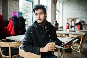 Casual and stylish young asian man with earphones at cafe drinking juice from glass and holding tablet. photo