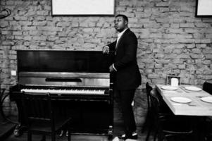 Strong powerful african american man in black suit standing against piano. photo