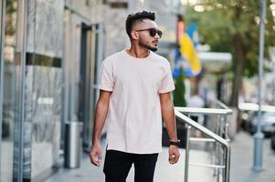 Stylish indian beard man at sunglasses and pink t-shirt. India model posed outdoor at streets of city. photo