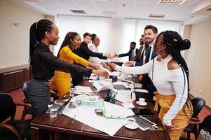 buen negocio. equipo de negocios multirracial que se dirige a la reunión alrededor de la mesa de juntas y se da la mano. foto