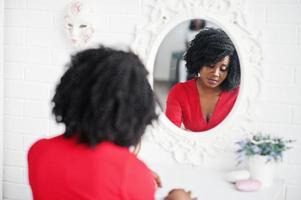 Fashion african american model in red beauty dress, sexy woman posing evening gown and looking at mirror. photo