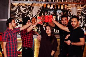 Group of indian friends having fun and rest at night club, drinking cocktails, clinking and cheers near bar counter. photo