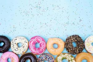 assorted donuts with chocolate frosting, topping sprinkles donuts Colorful variety and Variety of flavors mix of multi colored sweet donuts with frosted sprinkled on blue background. top view photo