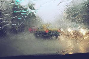 Drops Of Rain Drizzle on the glass windshield in the evening. street in the heavy rain. Bokeh Tail light and Traffic lights in city. Please drive  car carefully, slippery road. soft focus. photo