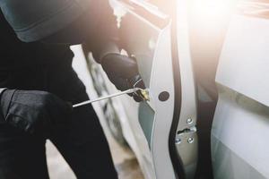 Close up car thief wearing black clothes hand holding screwdriver tamper yank and glove stealing automobile trying door handle to see if vehicle is unlocked  trying to break into. car theft concept. photo