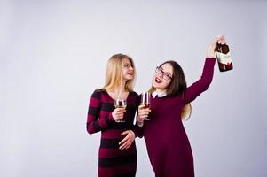 Two attractive friends in purple dresses drink sparkling wine or champagne in the studio. photo