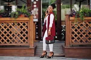 chica afroamericana con bolso de mano posada al aire libre de la ciudad de steets y hablando por teléfono. foto