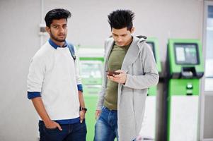 Two asian guys looking at mobile phone against row of green ATM. photo